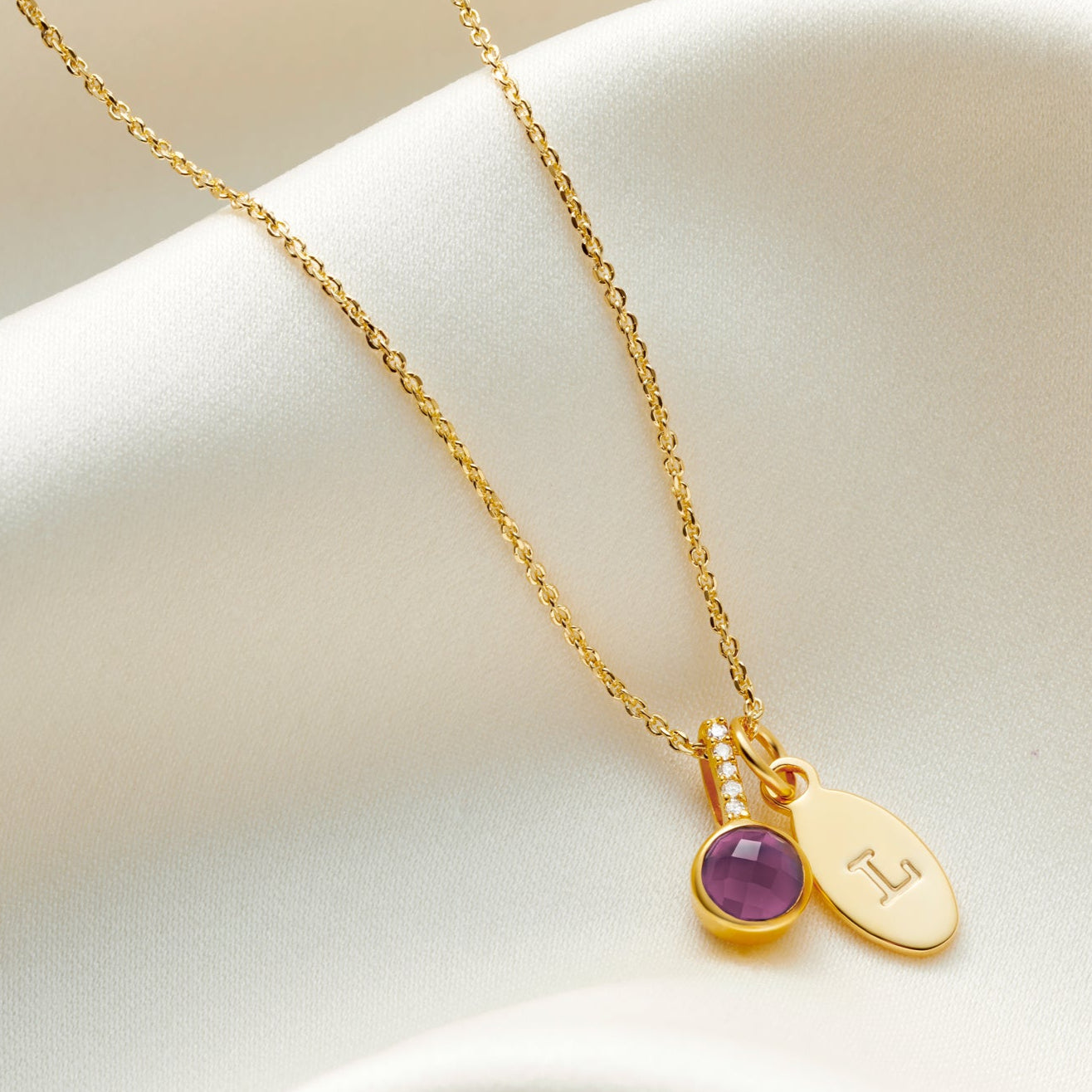 Faceted amethyst pendant with tiny white diamonds in the bale. Pendant is set in gold vermeil and hung on a fine trace chain alongside an oval charm, personalised with the letter L