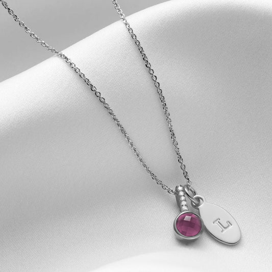 Faceted round amethyst pendant in a rub over setting with five tiny white diamonds in the bale.  Pendant is sterling silver and is hung on a fine silver trace chain along side an oval charm hand stamped with a capital letter L.