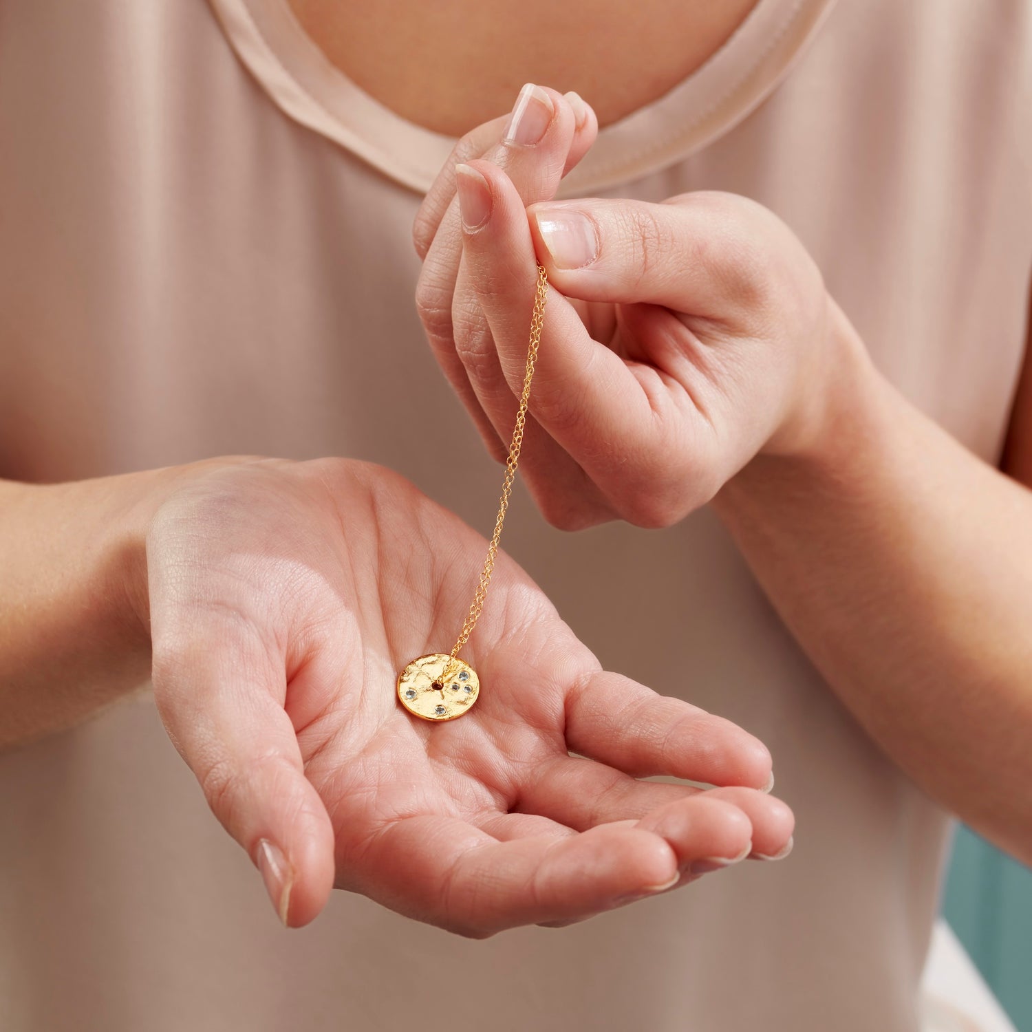 Pair of hands holding a textured gold spinner disc pendant set with small faceted aquamarine birthstone gems on a fine gold vermeil chain