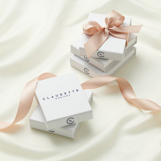 A pile of Claudette Worters white gift boxes for jewellery with the Claudette Worters logo on the front, tied with pretty blush pink satin ribbons.