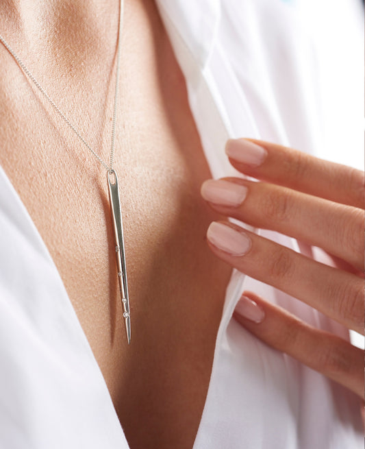 Woman wearing a long thin spike pendant necklace in sterling silver with tiny white crystals depicting the layout of the Aries star constellation on a fine silver chain