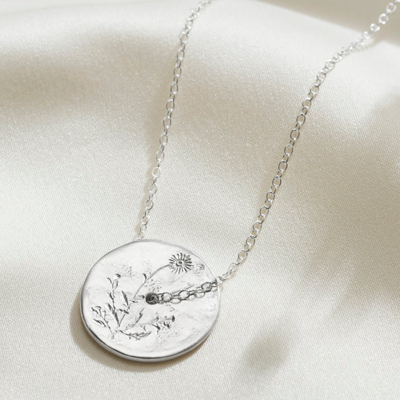 Hand engraved daisy birth flower on a sterling silver disc pendant with a hole in the middle and a fine trace chain slotting through the middle.