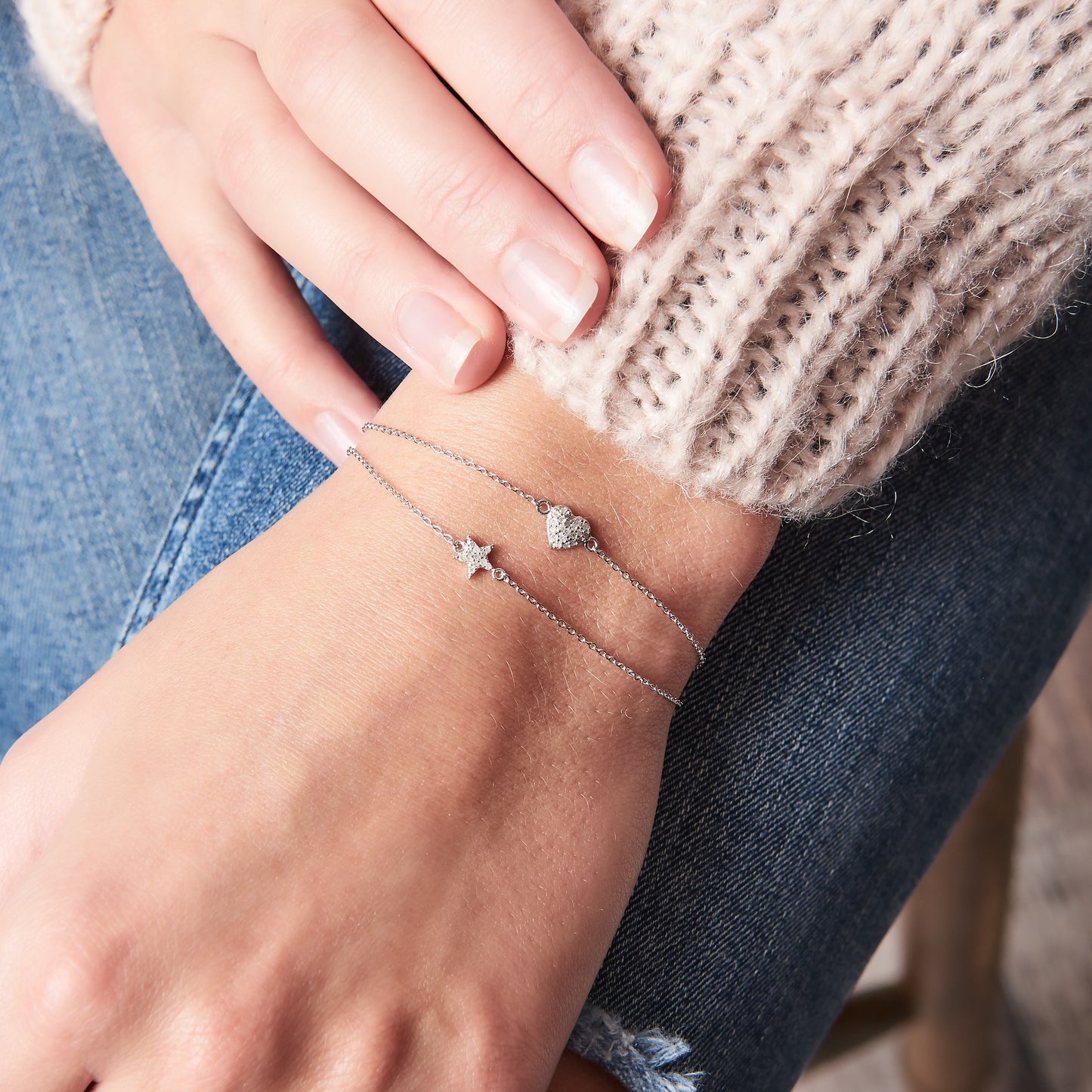 Woman wearing two diamond bracelets. One bracelet has a heart charm set with tiny white diamonds and the other one has a little star set with tiny white diamonds. Both bracelets have fine sterling silver trace chains. By Claudette Worters Jewellery.