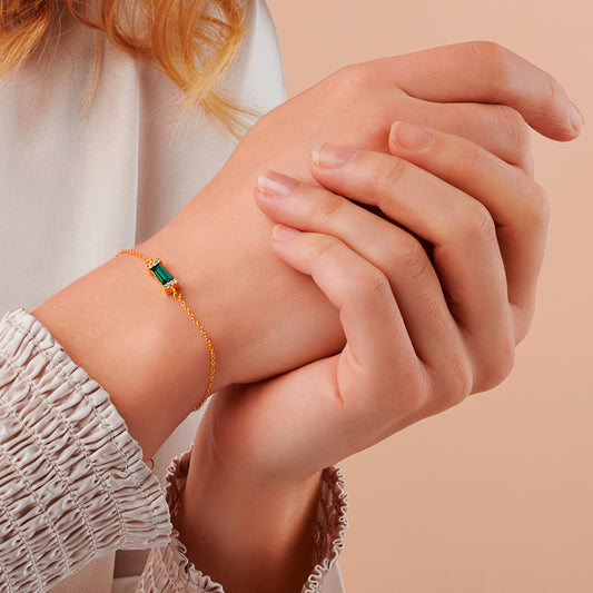 Dainty emerald birthstone bracelet in gold with green baguette gemstone on a fine gold trace chain by Claudette Worters.