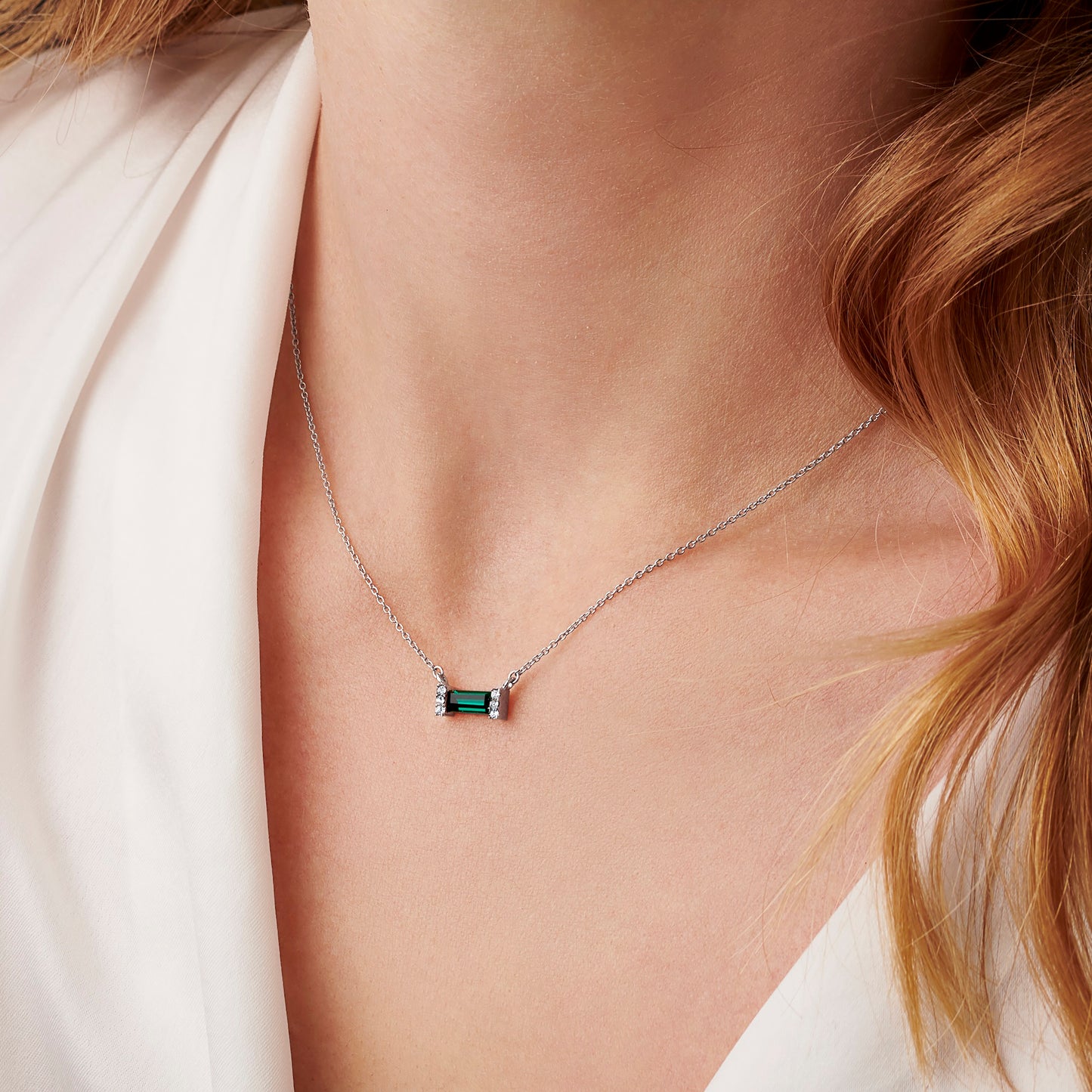 Woman wearing a green emerald baguette shaped crystal set in sterling silver on a fine silver trace chain.