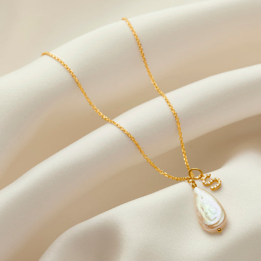 Teardrop shaped freshwater pearl pendant with a diamond set initial charm necklace on a dainty gold trace chain.