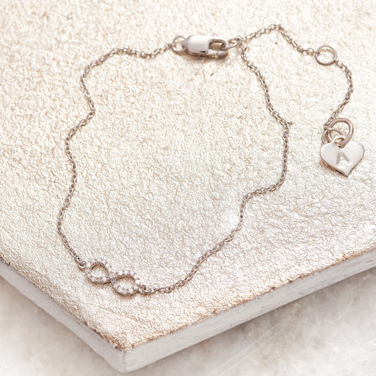 Dainty silver bracelet with a little infinity charm that has been set with tiny white diamonds.  The bracelet closes with a lobster claw fastening and has an extender chain.  On the end of the extender chain is a silver heart charm that has been hand stamped with the letter A