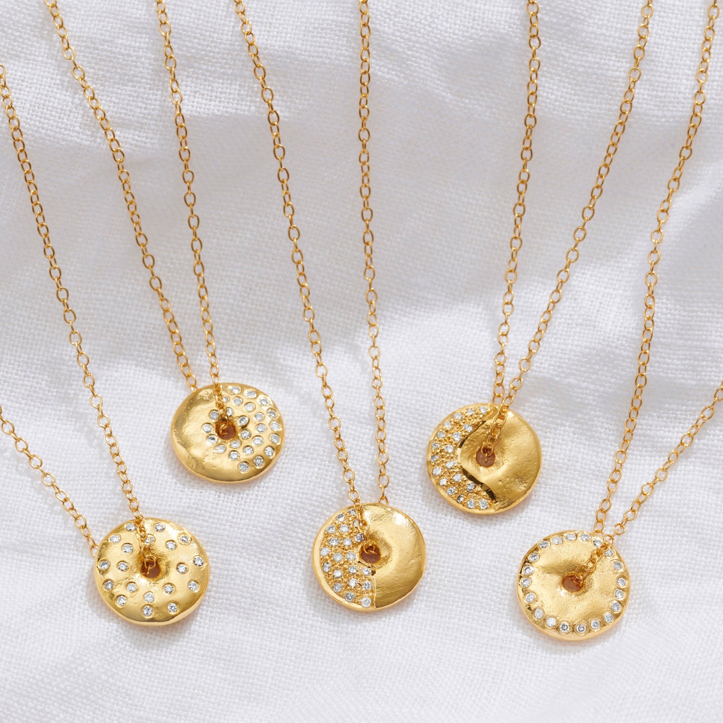 Gold moon phase necklaces with disc pendants set with diamonds representing each moon phase on fine gold trace chains by Claudette Worters.