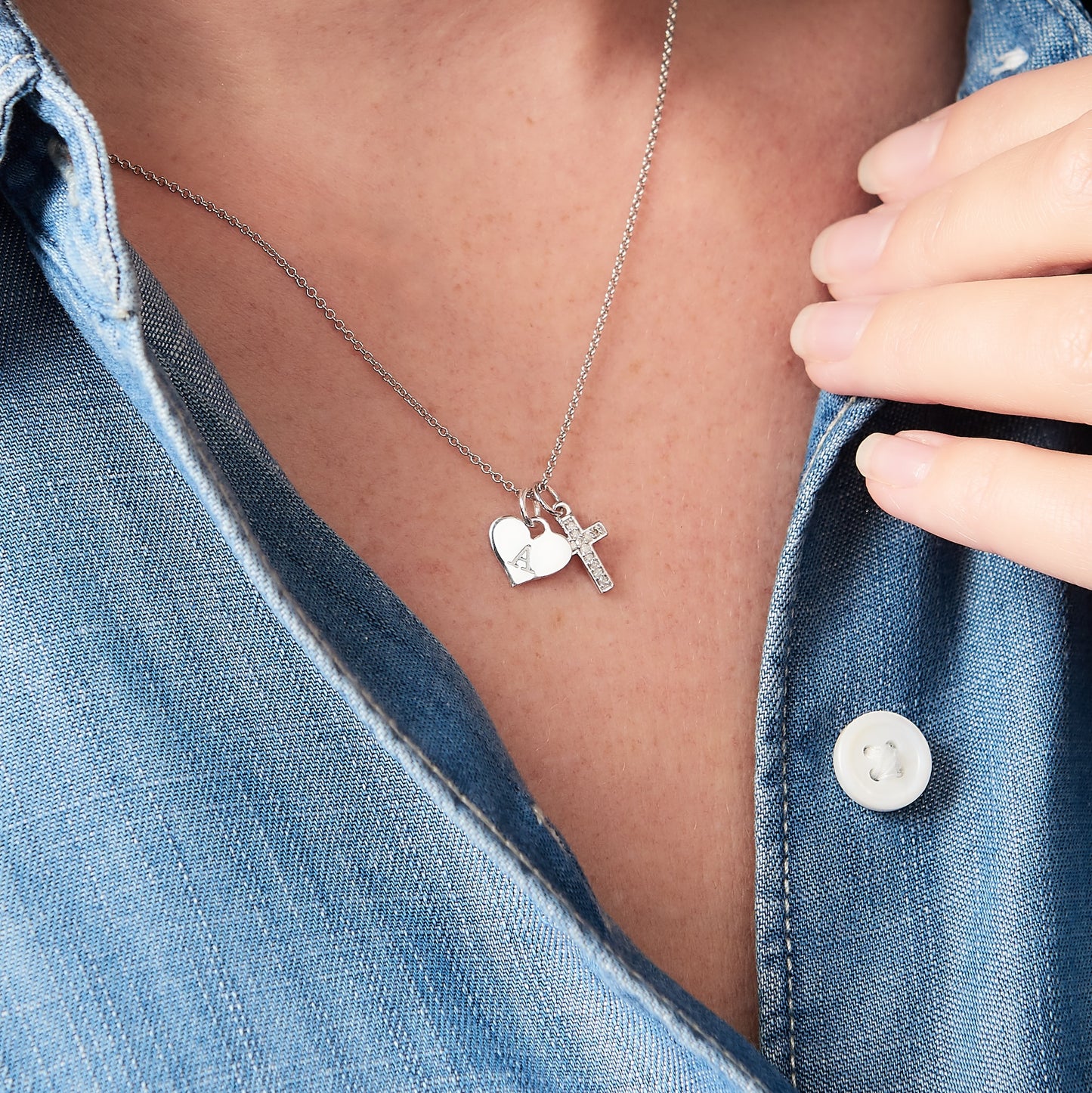 Tiny cross pendant set with little white diamonds with a sterling silver heart charm hand stamped with the letter A. Pendants are hung on a fine sterling silver trace chain. By Claudette Worters Jewellery.