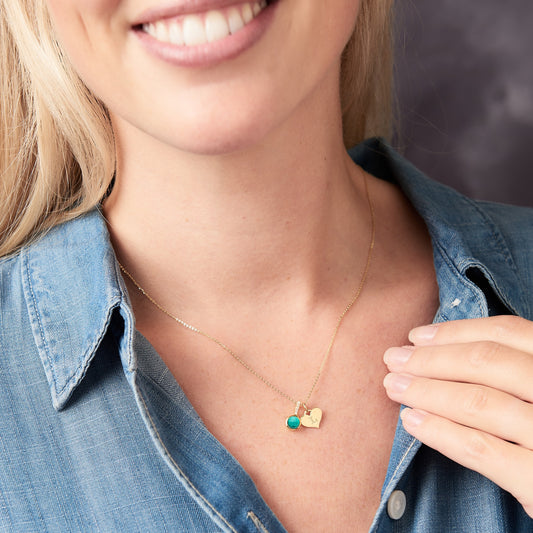 Woman wearing a gold necklace with a turquoise birthstone pendant set with little white diamonds and heart-shaped charm hand stamped with an initial, smiling.