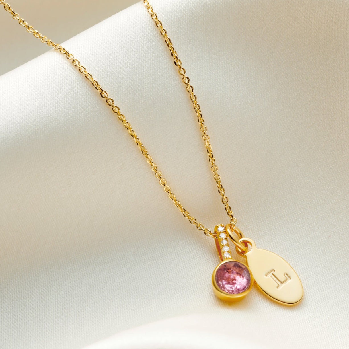 Faceted Pink Tourmaline birthstone pendant in 18 carat yellow gold vermeil with little white diamonds in the bale. Pendant is on a fine trace chain with an oval charm personalised with a capital letter L.