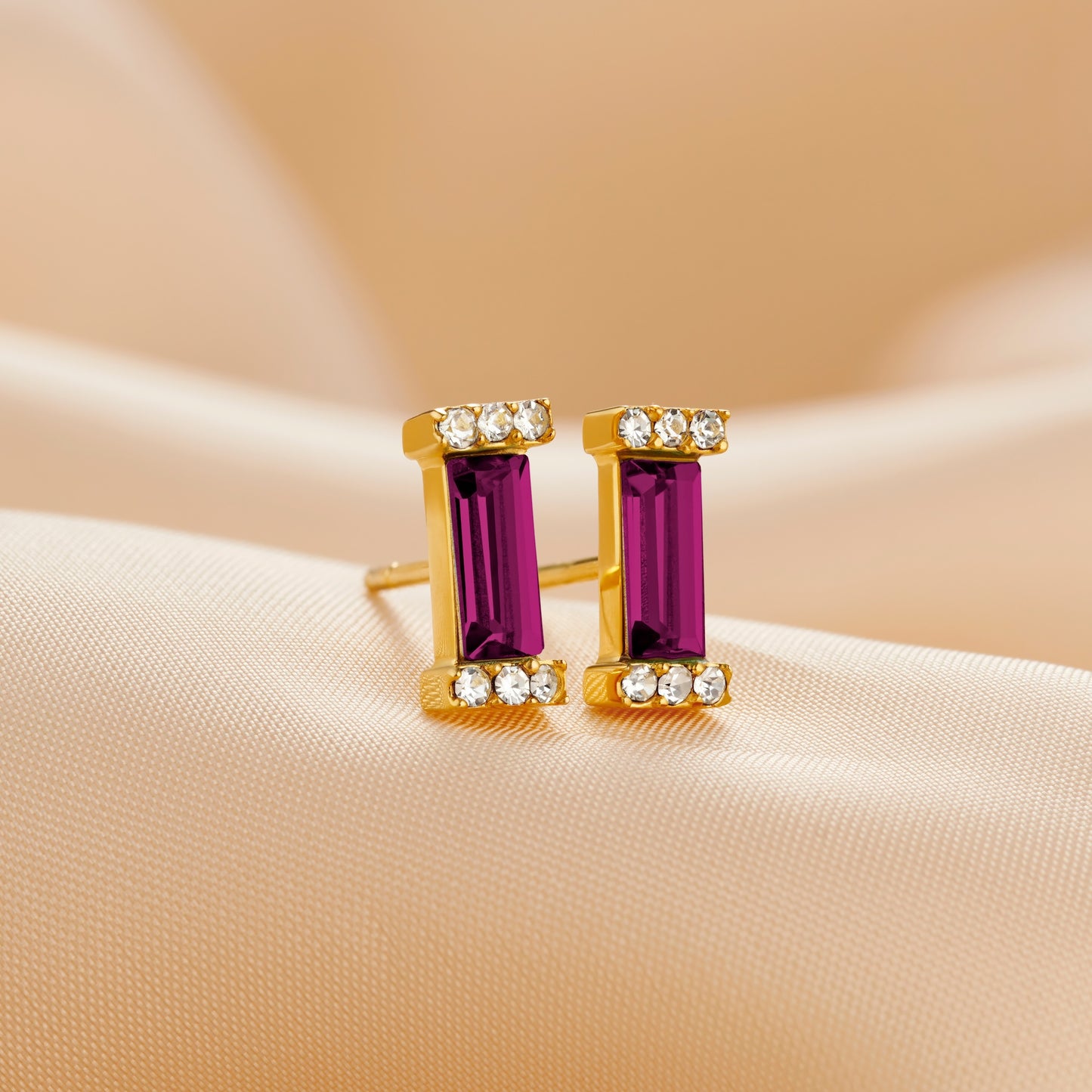 Gold stud earring set with an amethyst baguette cut Swarovski crystal topped with pavé set clear crystals in the ends of each stone setting by Claudette Worters.