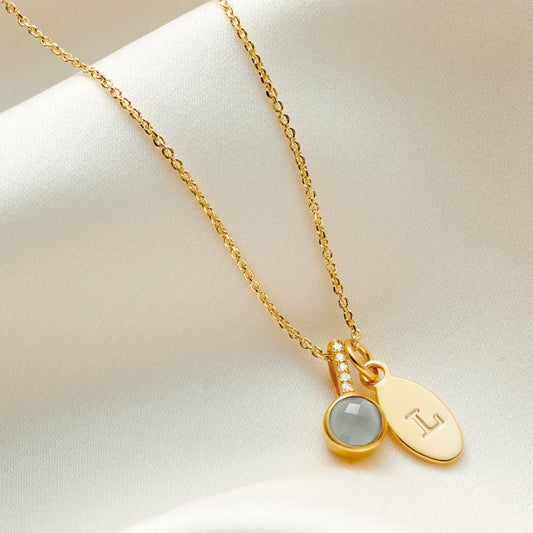 Faceted aquamarine birthstone pendant necklace with white diamonds in the bale with oval charm personalised with the letter L in gold vermeil.