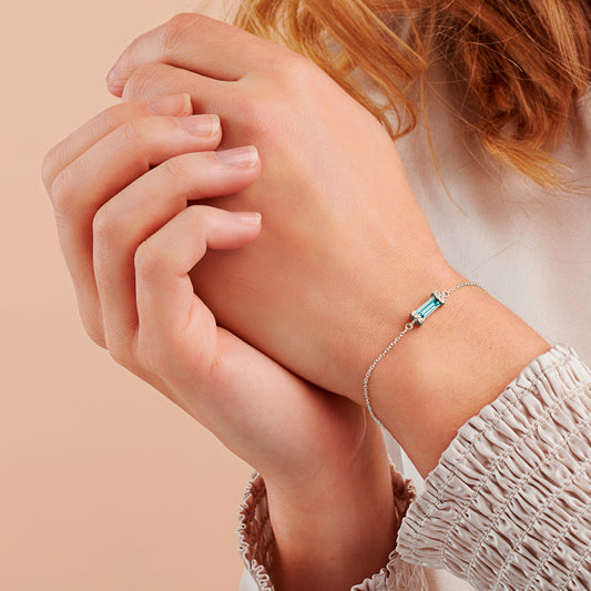 Woman wearing a bracelet on her wrist with an aquamarine coloured baguette crystal in a sterling silver pavé setting on a fine sterling silver trace chain.