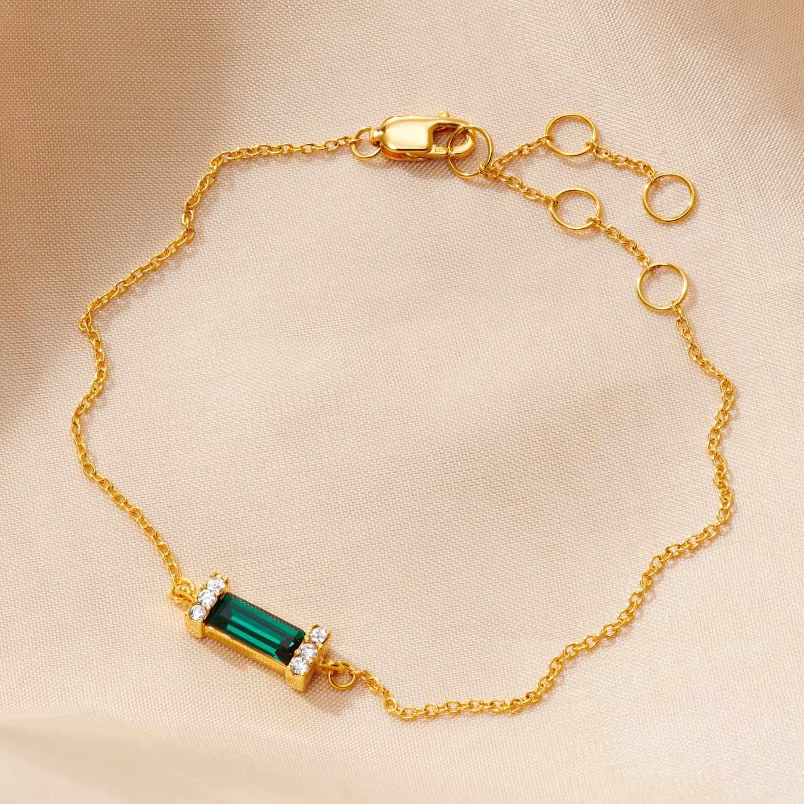 Gold bracelet with an emerald green faceted baguette stone in the middle on a fine gold trace chain with a lobster claw fastening.