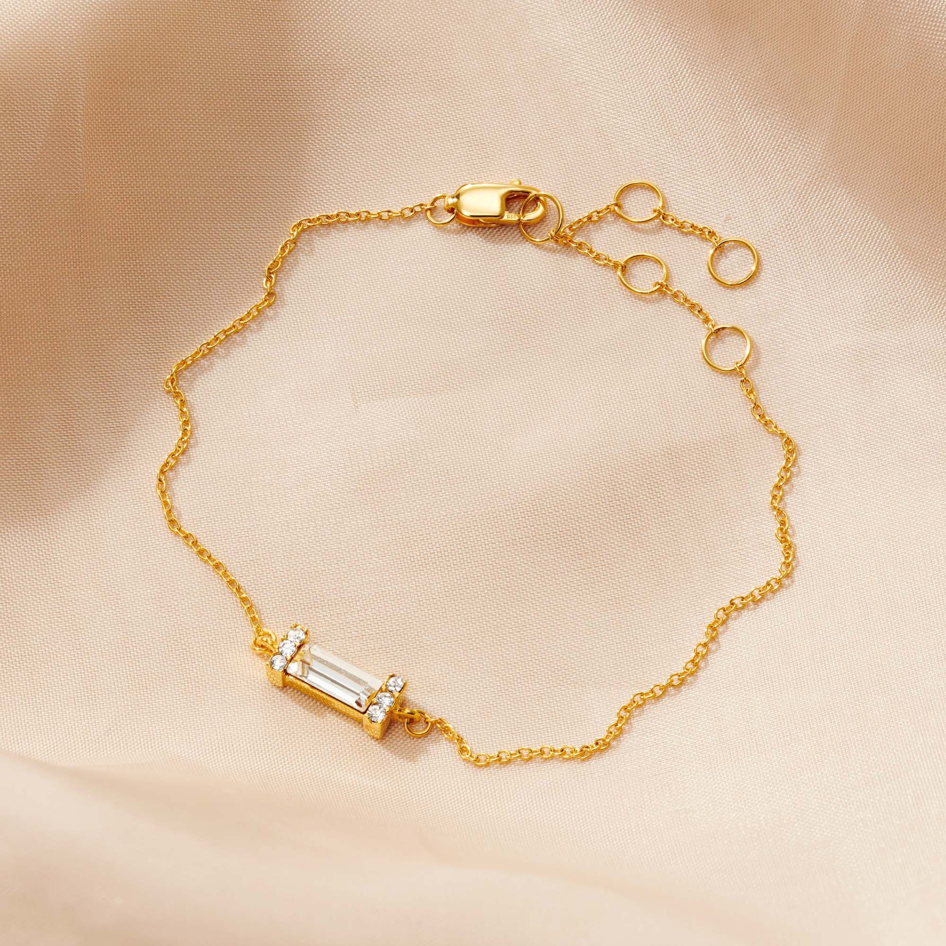 Pretty birthstone bracelet in gold with a baguette cut clear crystal in a contemporary Art Deco style setting.  The bracelet has a dainty trace chain and fastens with a lobster claw and is adjustable.  By Claudette Worters.