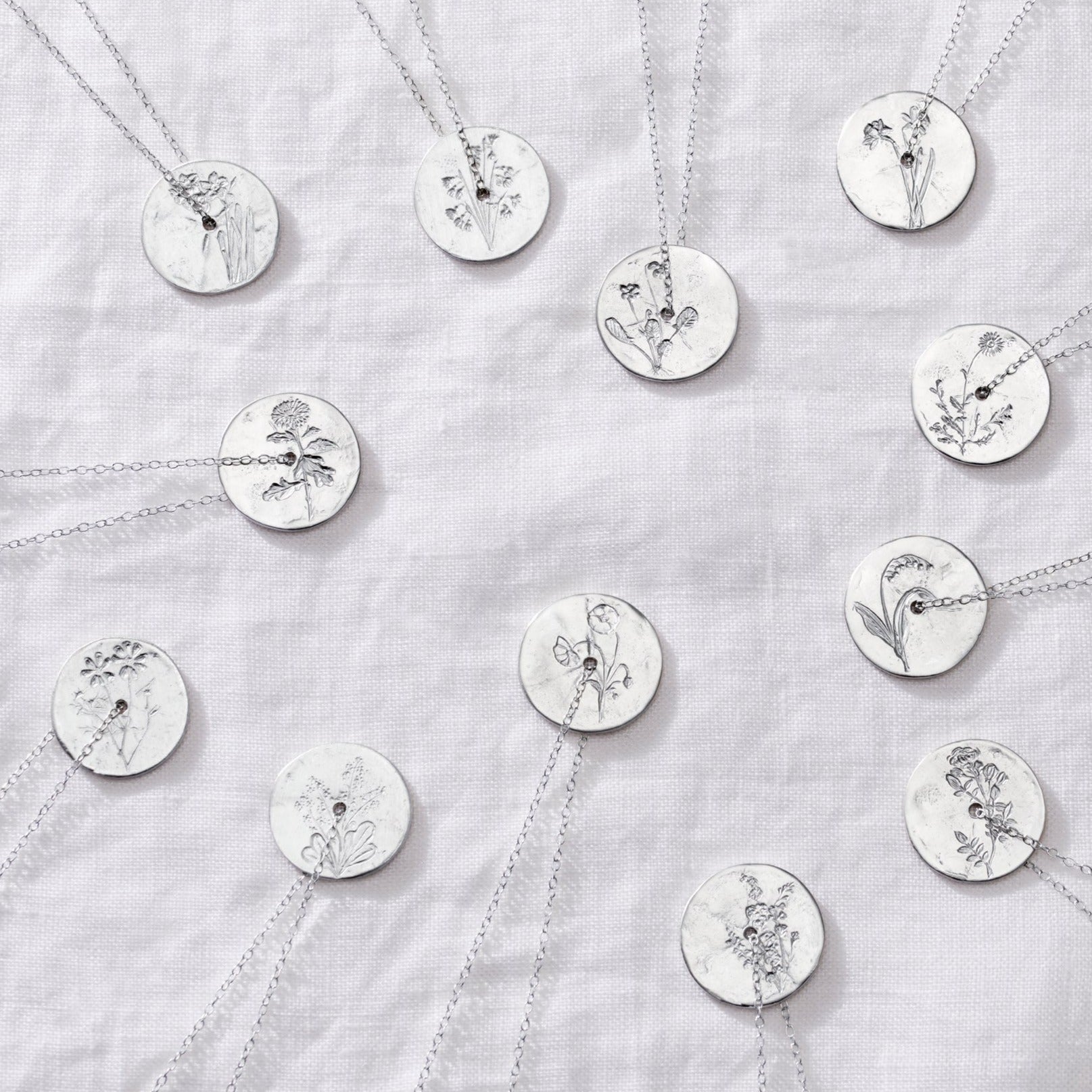 Birth flower necklaces featuring hand engraved spinner disc pendants on trace chains in recycled sterling silver by Claudette Worters