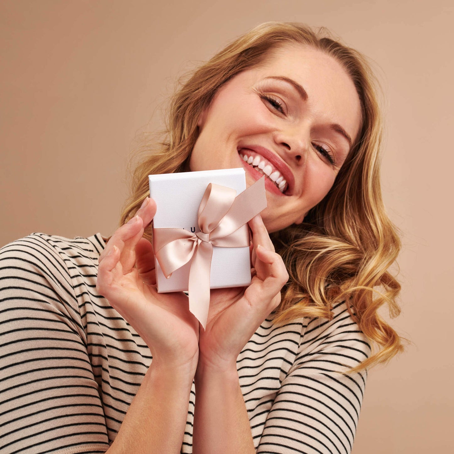 Claudette Worters white jewellery gift box tied with a blush pink satin ribbon held by a pretty smiling lady.