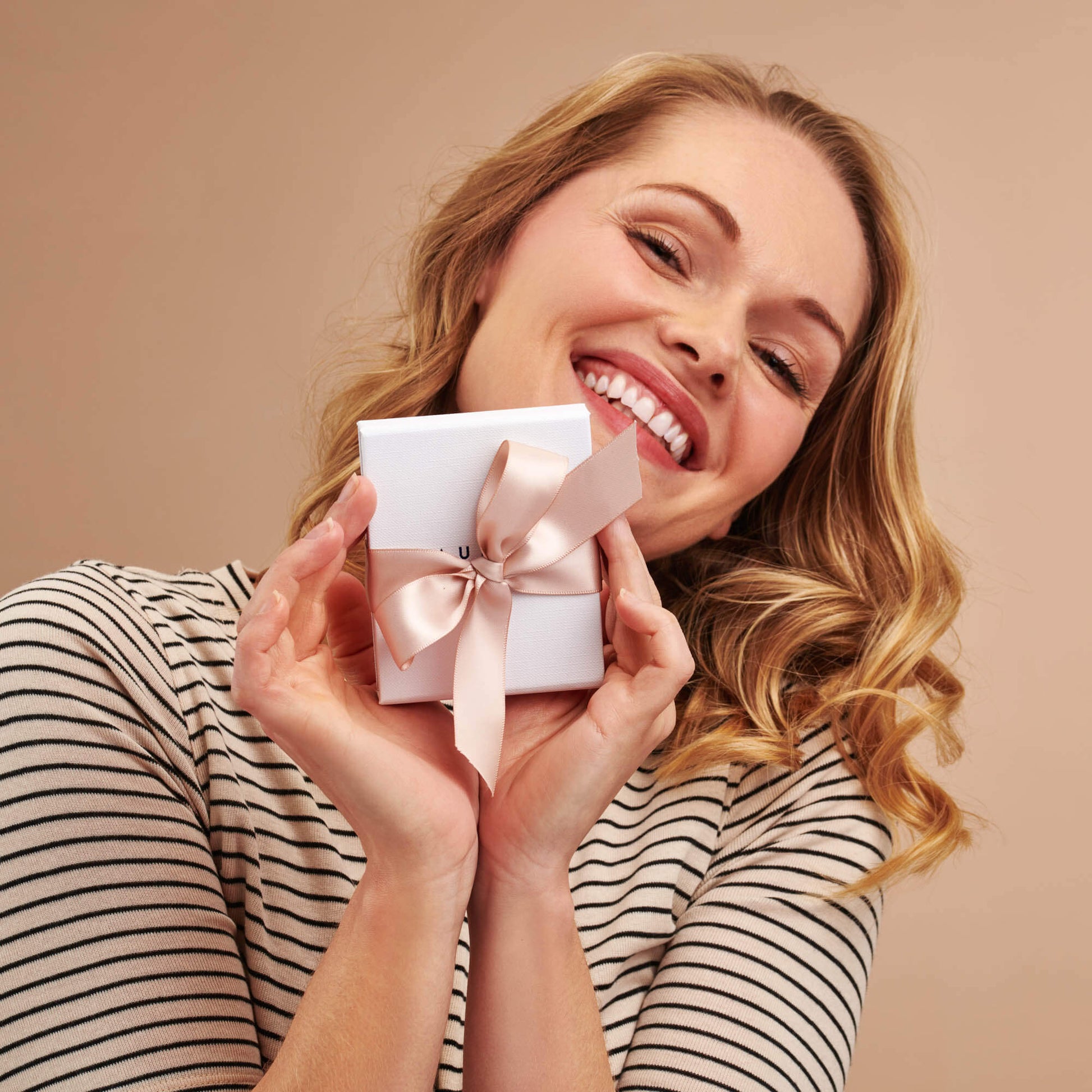 Claudette Worters white jewellery gift box tied with a blush pink satin ribbon held by a pretty smiling lady.