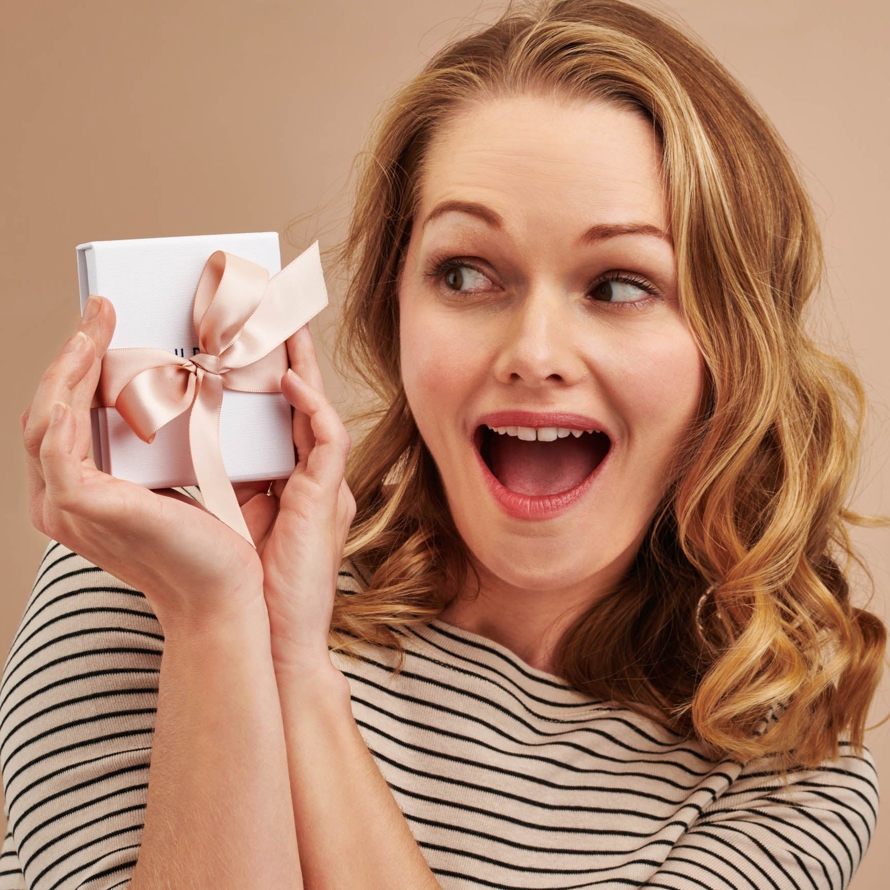 Lady in striped T-shirt looking pleased holding a small white gift box, tied with a pink satin ribbon.