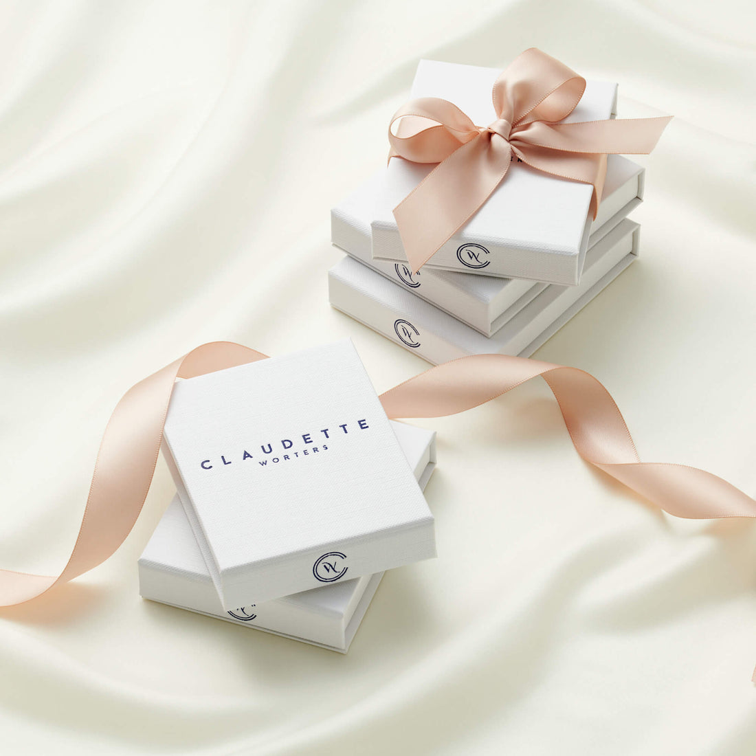 Stacks of white jewellery boxes with the Claudette Worters logo on the front, tied with a blush pink ribbon.