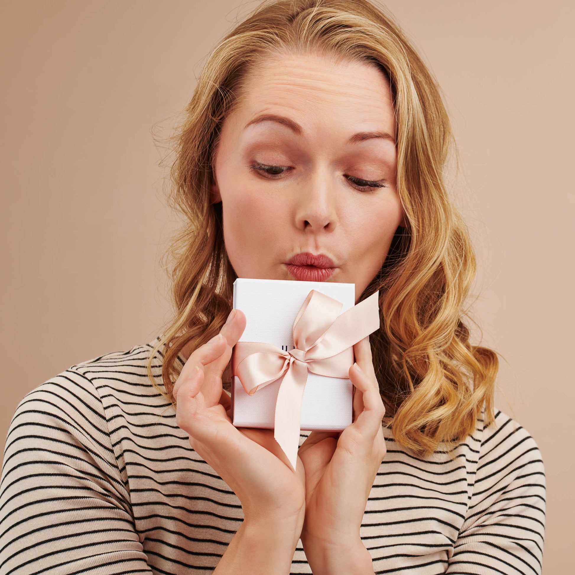 Woman in Breton striped tee holding a white gift box tied with a nude satin ribbon.