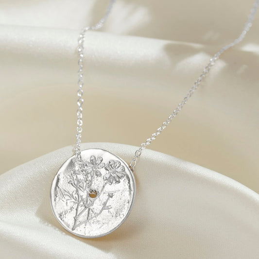 Silver disc necklace with a soft brushed sateen finish with hand engraved cosmos flowers on the surface.  The circular pendant has a hole in the middle and a dainty sterling  silver trace chain is threaded through the centre.