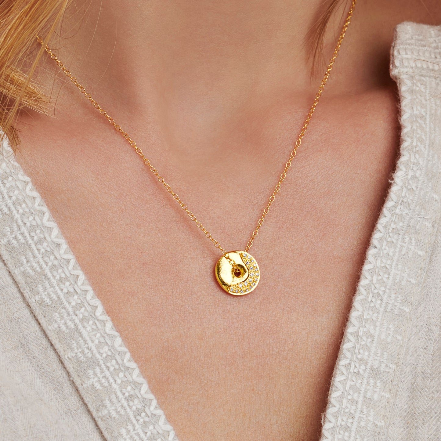 Model wearing gold vermeil waxing crescent moon phase pendant necklace by Claudette Worters, showing organic lunar texture and real diamonds on a rotating disc pendant.