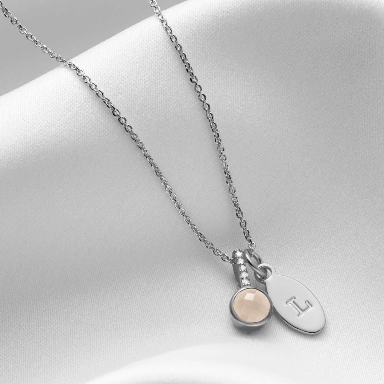 Faceted round rock crystal pendant in a rub over setting with a row of tiny diamonds in the bale.  The pendant is hung alongside a personalised oval charm.  Hung on a fine trace chain that's been rhodium plated by Claudette Worters 
