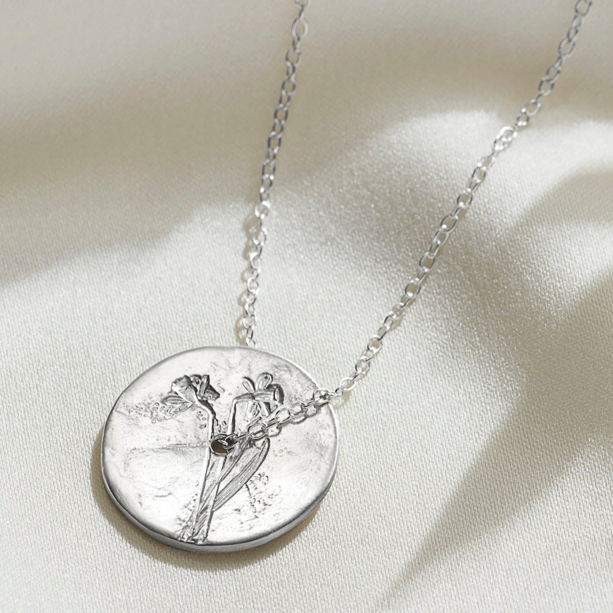 Sterling  silver spinner disc necklace with hand engraved daffodil, the March birth flower.  The pendant has a hole in the middle and a fine trace chain is threaded through the centre.