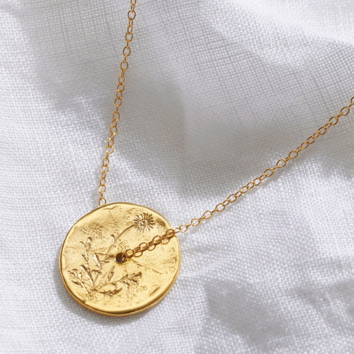 Gold birth flower necklace with a spinner disc pendant with hand engraved daisy motif for the month of April.  The circle pendant has a hole in the middle with a fine gold trace chain running through the centre of the piece.