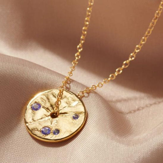 Gold disk pendant necklace set with purple Tanzanite birthstones.  A fine gold chain runs through the centre of the pendant.