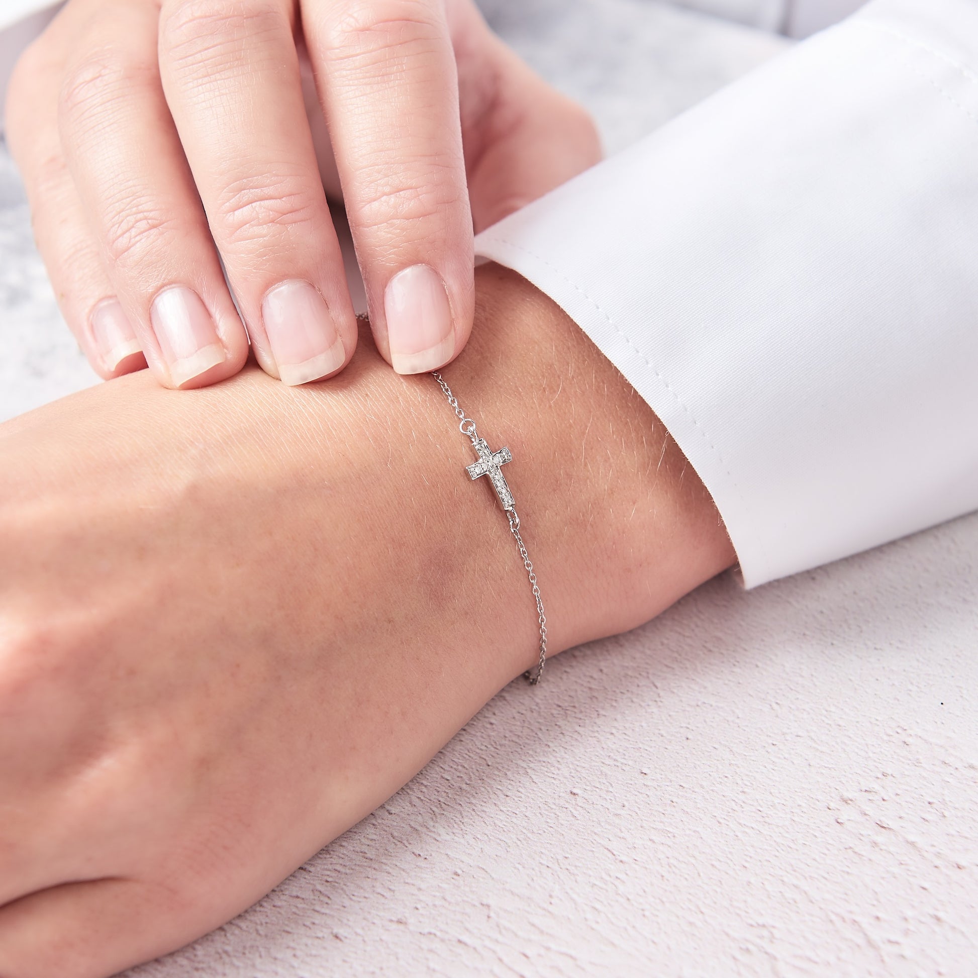 Dainty silver diamond cross bracelet on a fine silver trace chain.