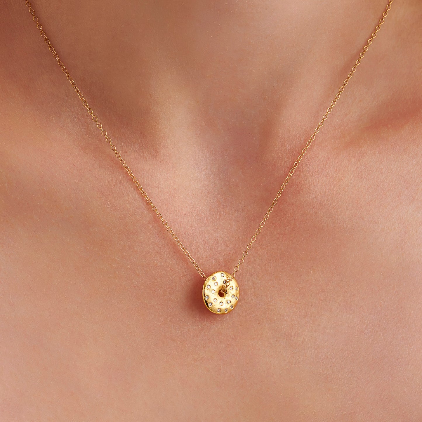 Organic gold vermeil moon phase necklace on model, set with natural diamonds on textured gold lunar disc pendant with a hole in the centre with a chain threaded through the centre by Claudette Worters.