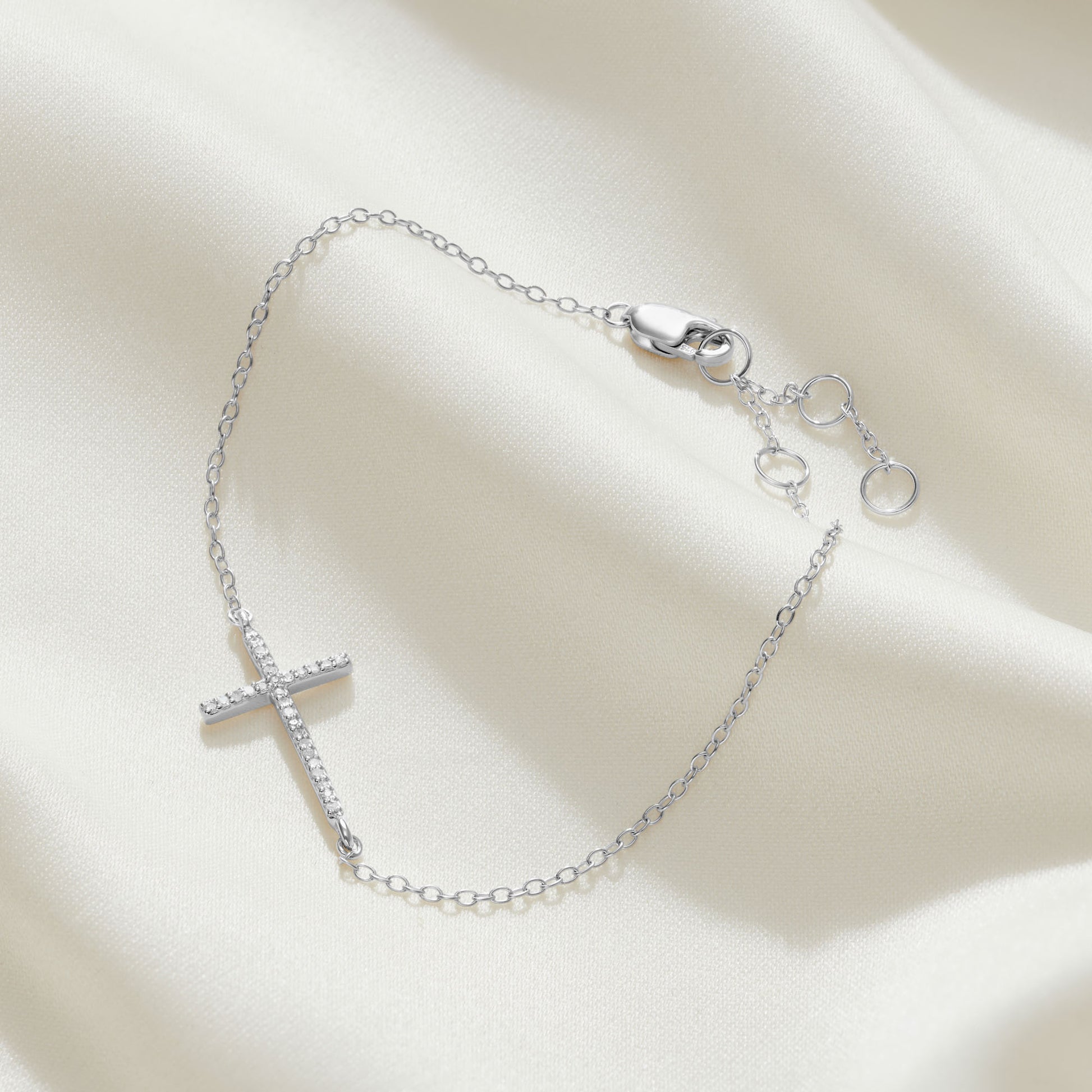 Sterling silver bracelet with a slim contemporary cross that runs sideways across the bracelet set with tiny white diamonds on a fine silver adjustable trace chain with a lobster claw fastening.