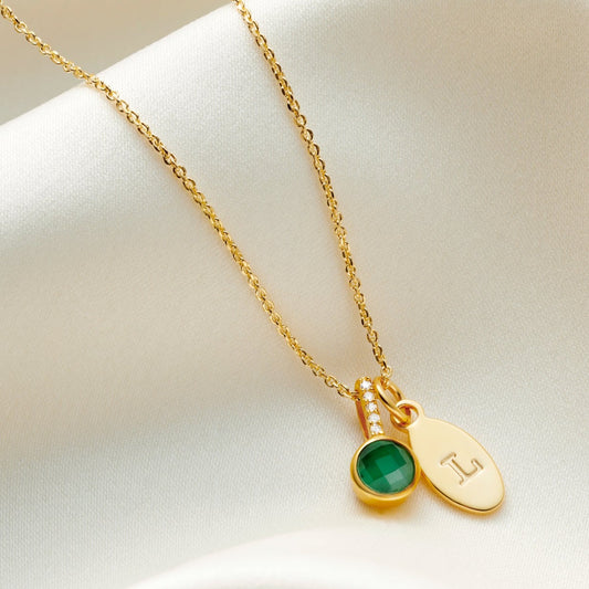 Faceted emerald pendant necklace in gold with a small oval charm personalised with the letter L on a fine trace chain.