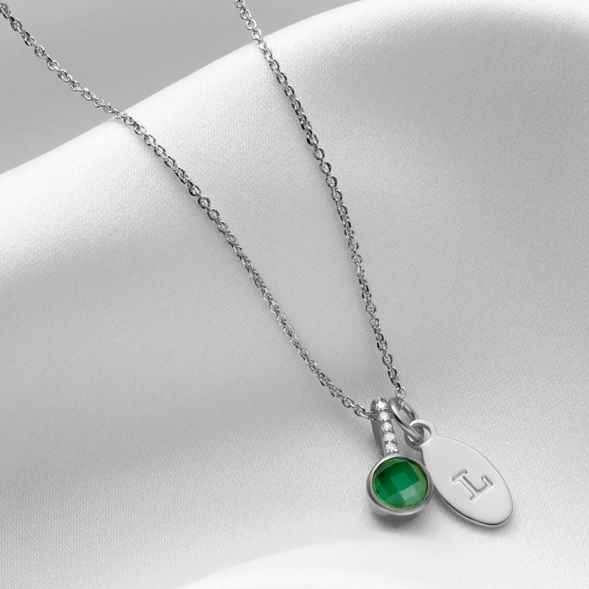 Emerald birthstone necklace in silver featuring a cushion cut green emerald in a sterling silver setting with tiny white diamonds in the bale. 