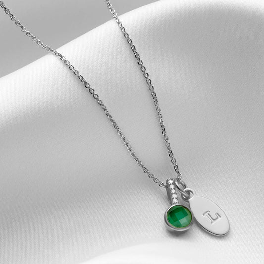 Emerald gemstone necklace in silver.  Necklace has a round, cushion cut green emerald in a sterling silver setting with tiny white diamonds in the bale.  There is a silver oval charm personalised with the letter L which is hung along side the emerald pendant on a fine sterling silver trace chain.  The piece is by Claudette Worters.