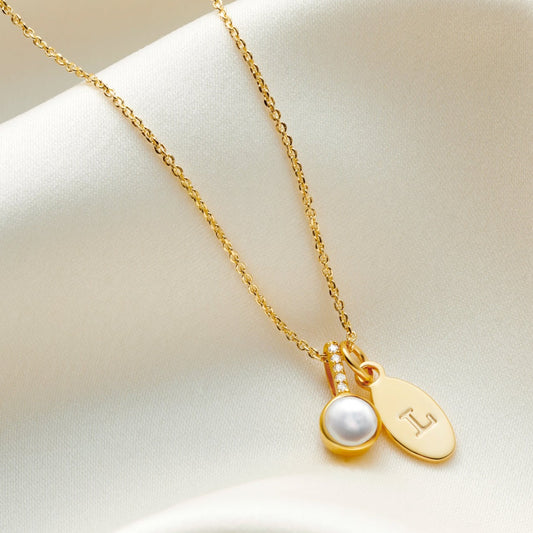 White freshwater pearl birthstone necklace in gold with tiny white diamonds in the bale and a small oval charm personalised with the letter L. 