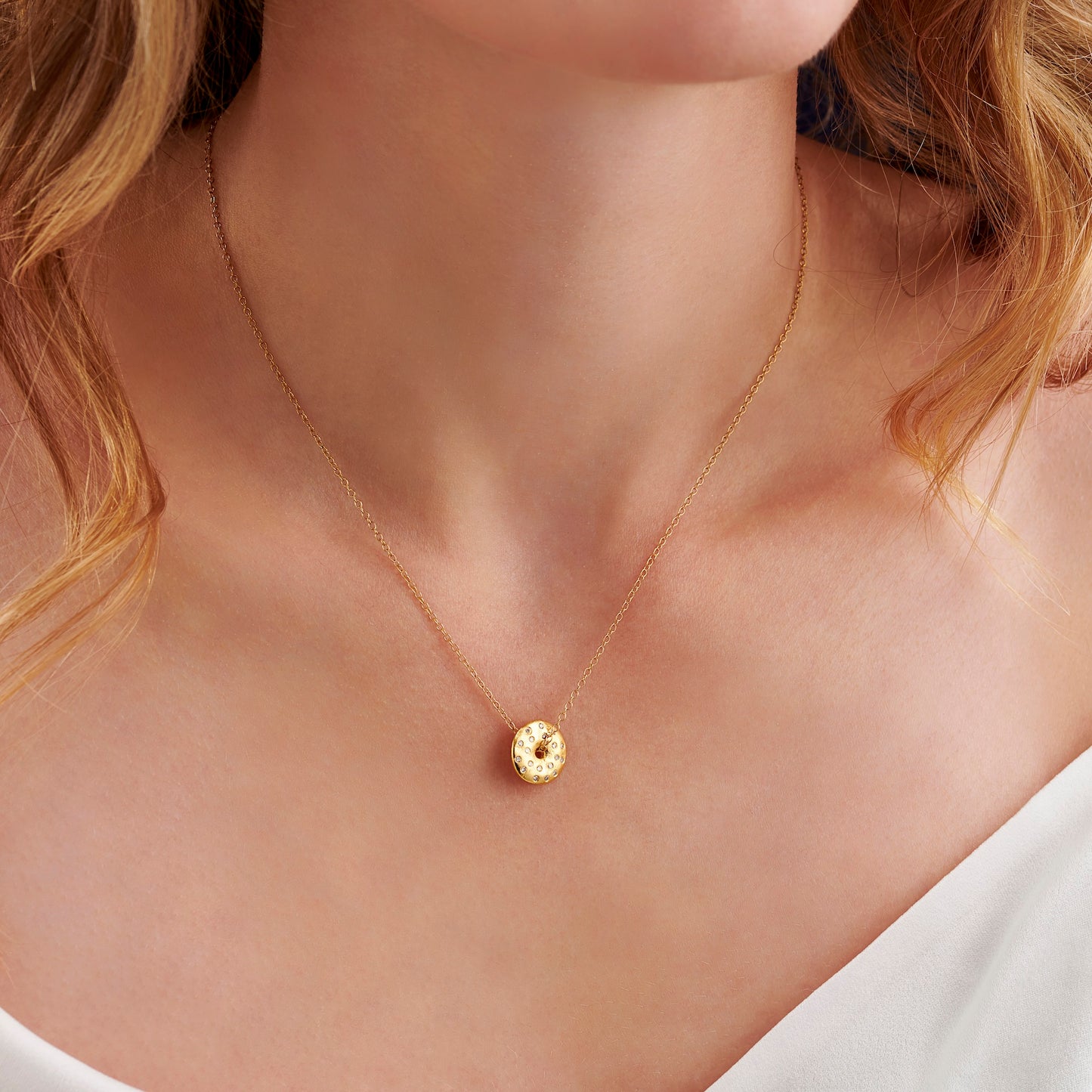 Gold necklace with a round pendant set with tiny round diamonds to signify a full moon on a woman wearing a white top.