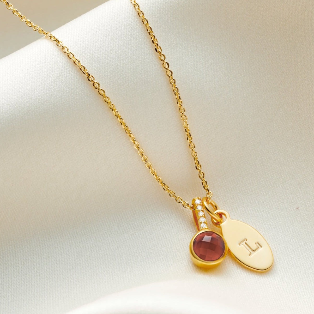 Faceted garnet birthstone pendant, in 18 carat gold vermeil with tiny white diamonds in the bale and an oval charm, personalised with the letter L.