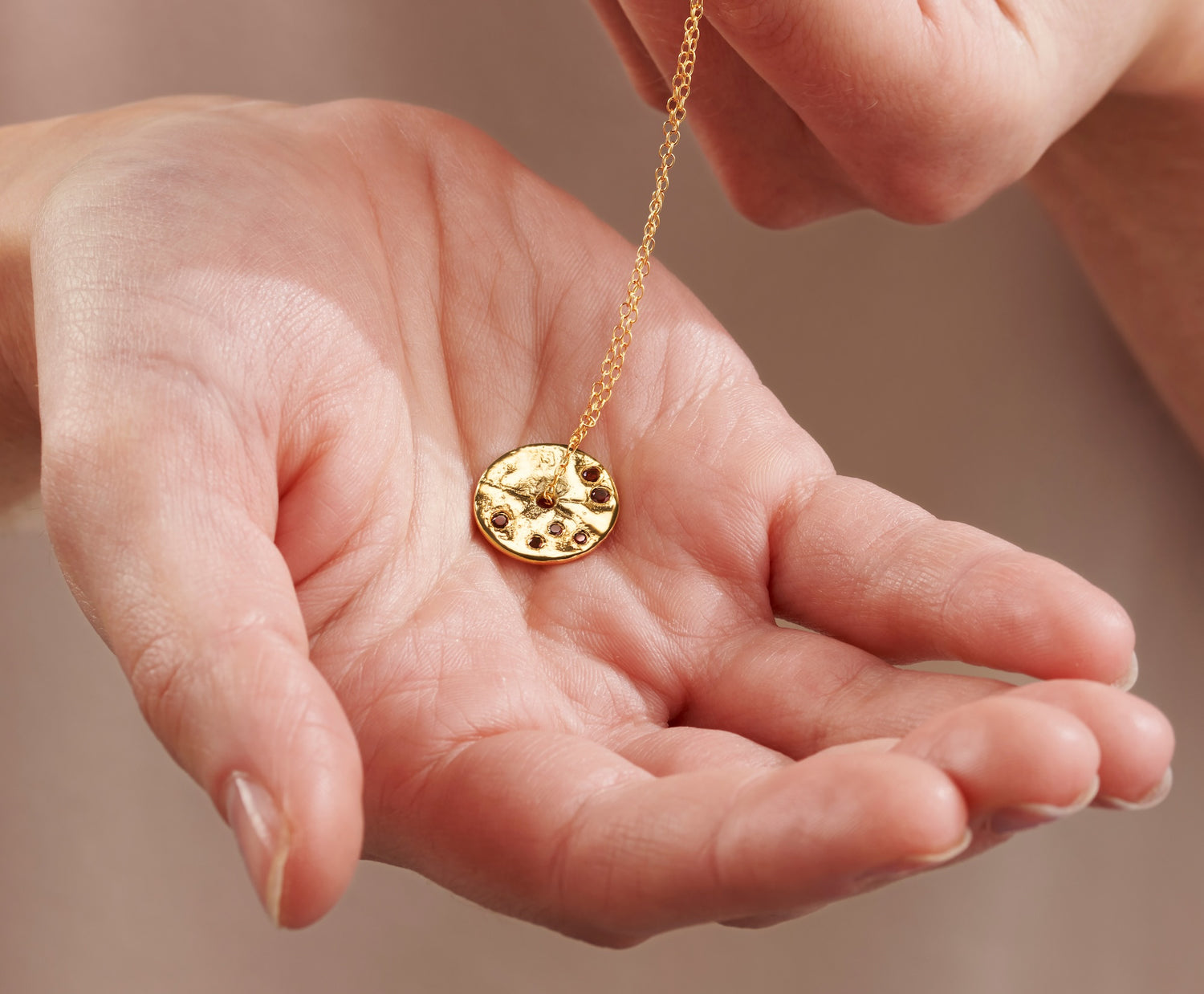 Gold textured disc spinner pendant on a fine gold vermeil trace chain with small round deep red garnets set into the surface by Claudette Worters.