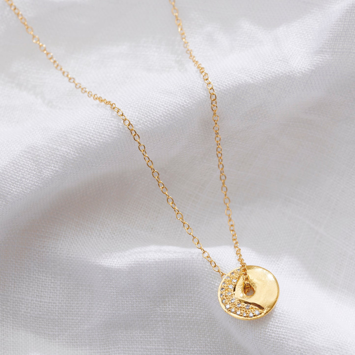 Gold vermeil Waning Crescent moon phase necklace by Claudette Worters. A small gold disc with a raised lunar texture. A curved line of tiny natural diamonds shows the moon phase. The chain threads through a central opening so the disc can spin freely.