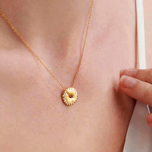 Gold moon phase necklace with a circular pendant with diamonds around the edge on a fine gold chain on woman's neck by Claudette Worters