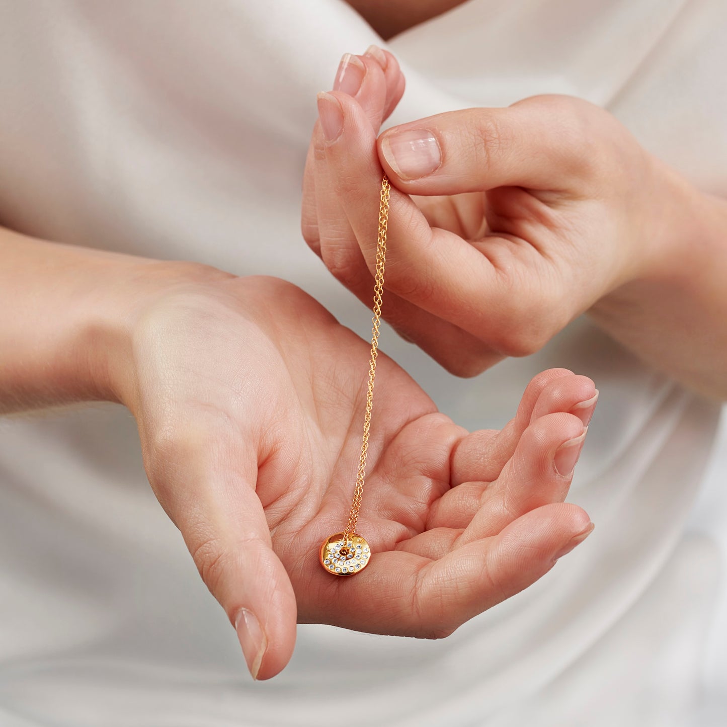 Gold moon phase necklace with a pendant held between two hands against a neutral background by Claudette Worters