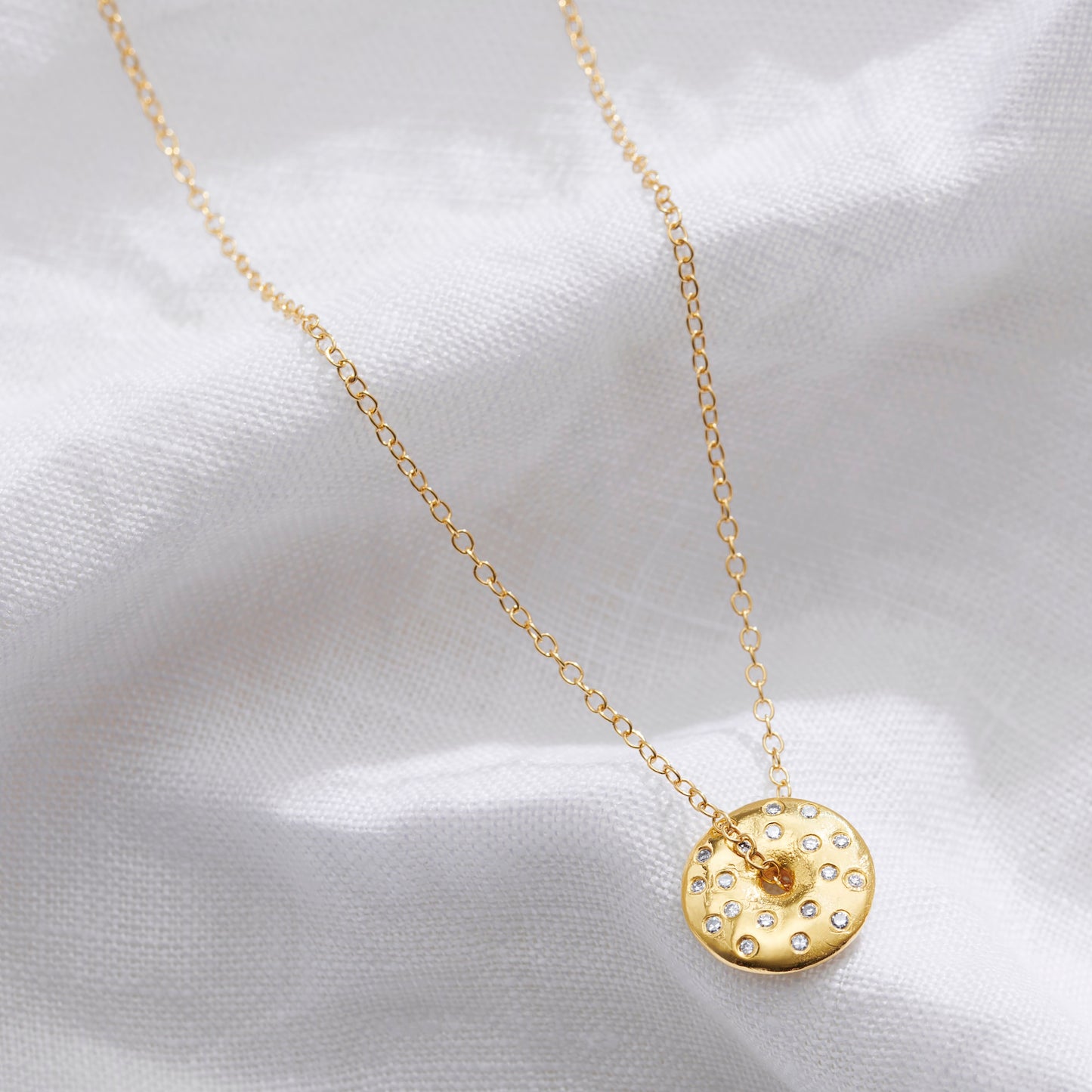  A dainty gold moon phase necklace set with diamonds featuring a disc spinner pendant on a fine gold chain by Claudette Worters