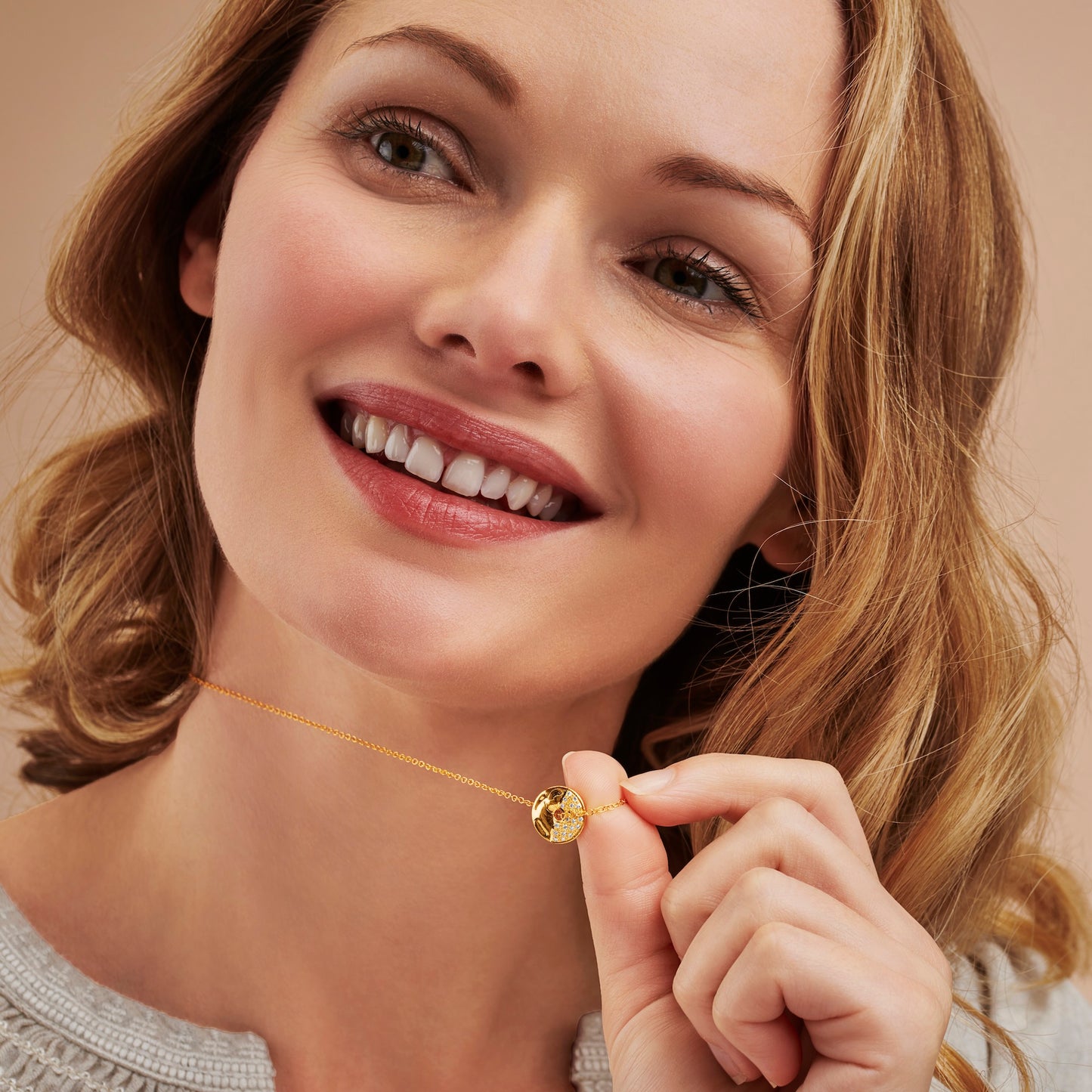Woman smiling holding a gold moon phase necklace featuring a gold circle pendant with one half set with real shite diamonds to represent the First Quarter moon phase on a fine gold chain by Claudette Worters