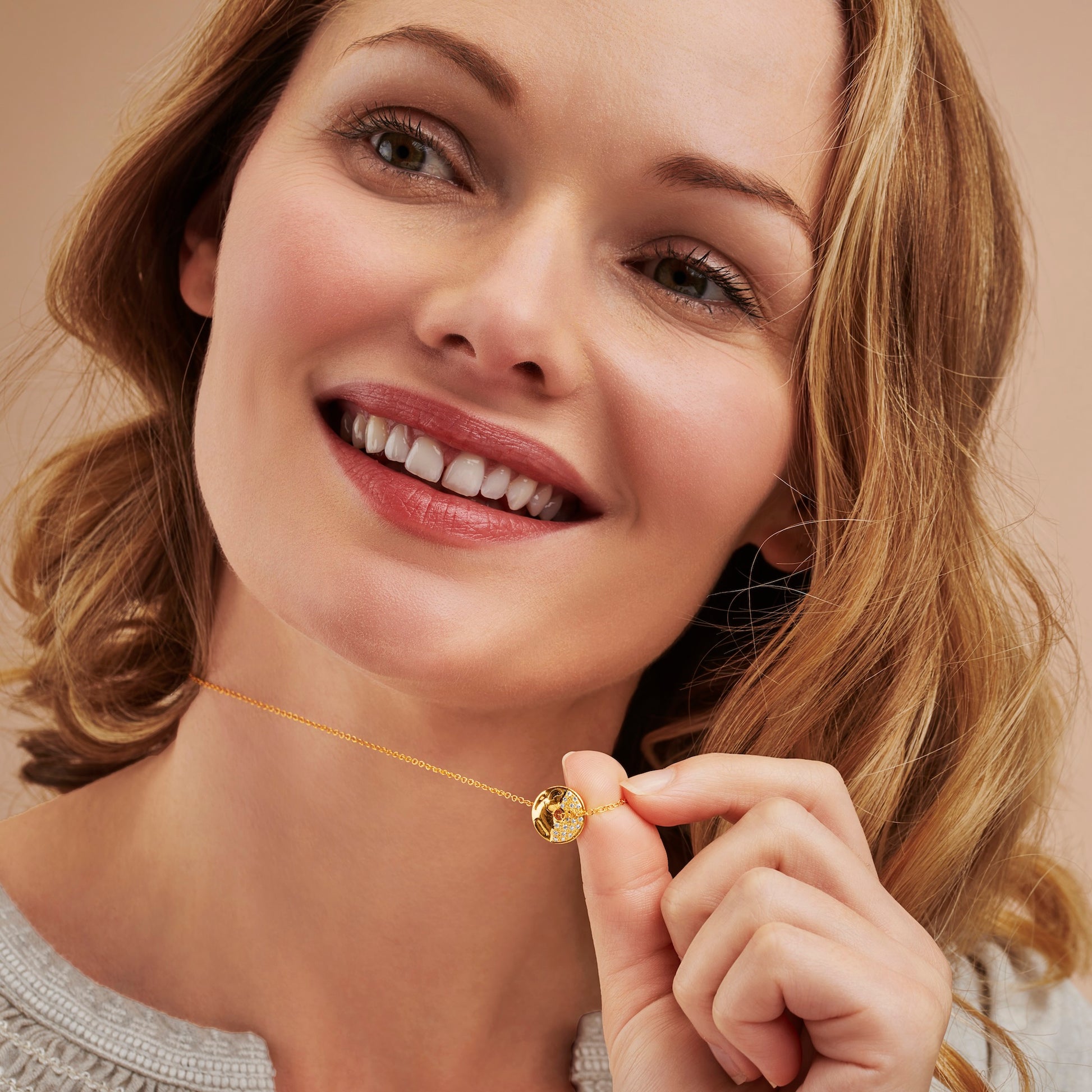 Woman smiling holding a gold moon phase necklace featuring a gold circle pendant with one half set with real shite diamonds to represent the First Quarter moon phase on a fine gold chain by Claudette Worters