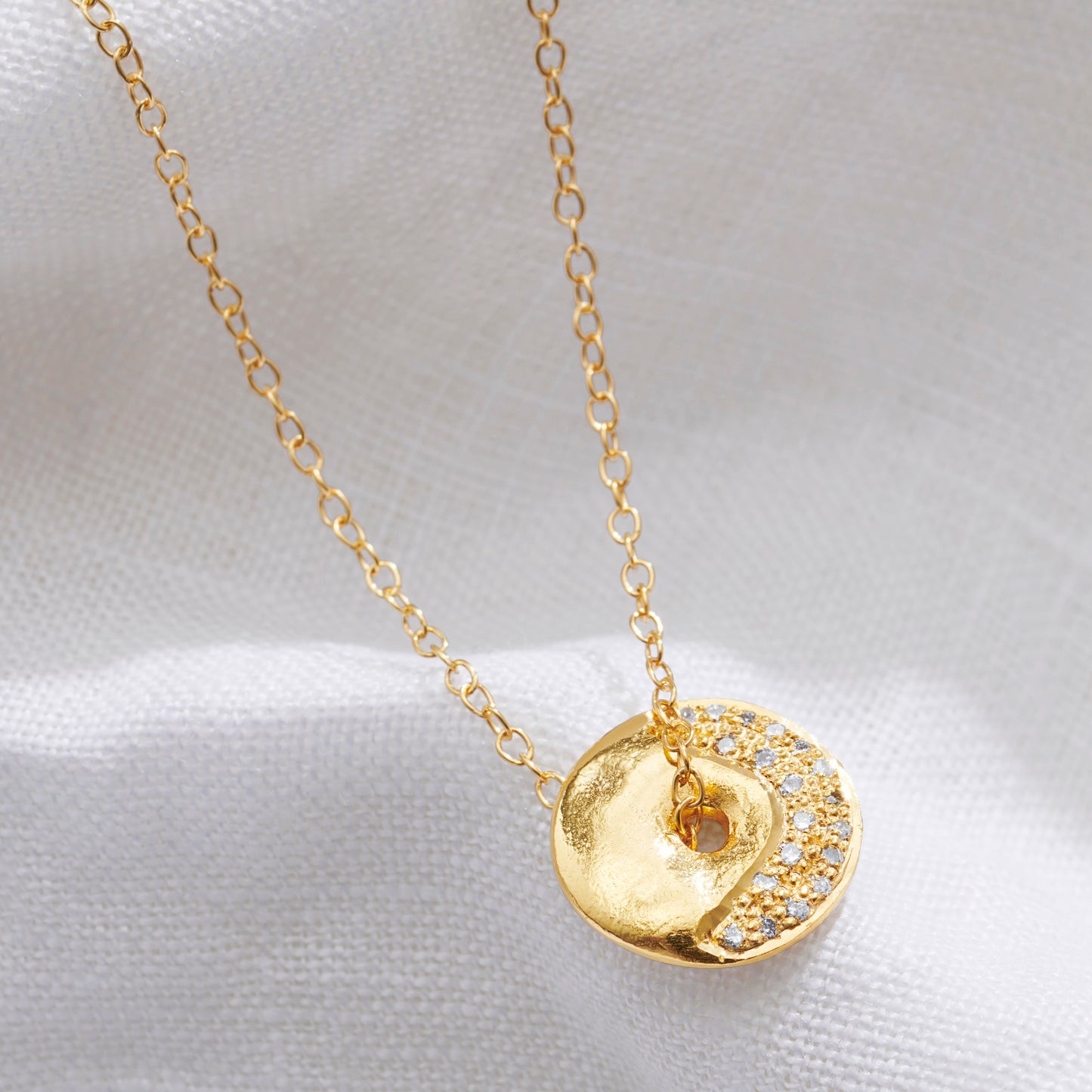 Textured gold disc pendant necklace with diamonds set in the pattern of a crescent moon on a fine gold trace chain