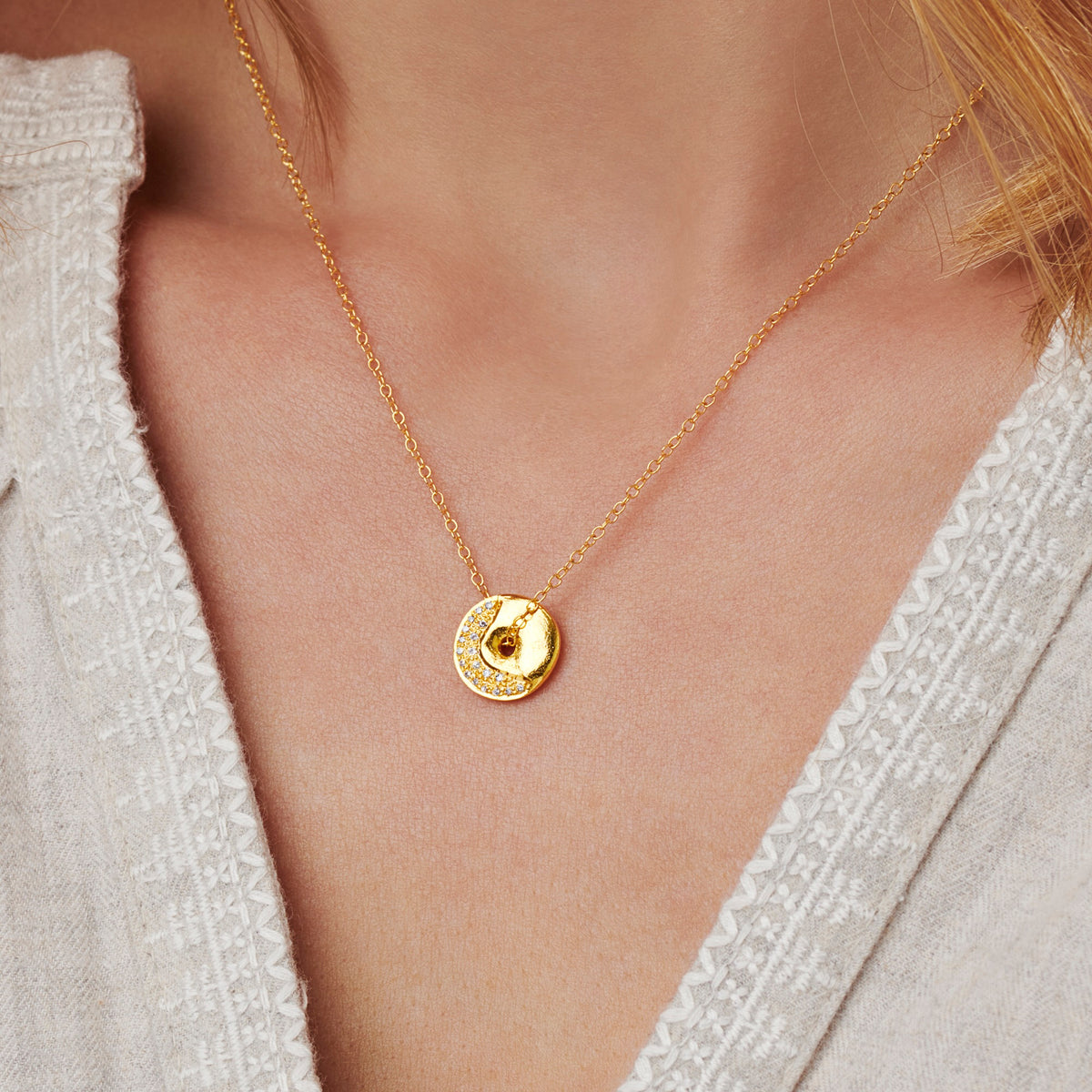 Gold moon phase necklace with a softly textured round pendant set with diamonds in the shape of a waning crescent moon worn on a delicate trace chain by Claudette Worters
